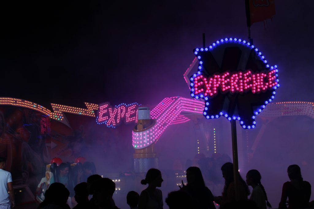 Crowds at Melilla's fair ground celebrating la Virgen de la Victoria, silhouetted in front of brightly lit amusement rides