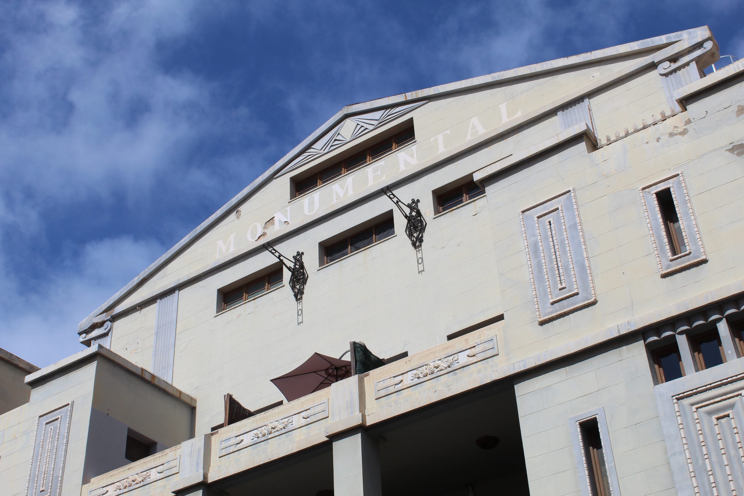 Grey Spanish building with art deco lines and details beneath a cloudy blue sky